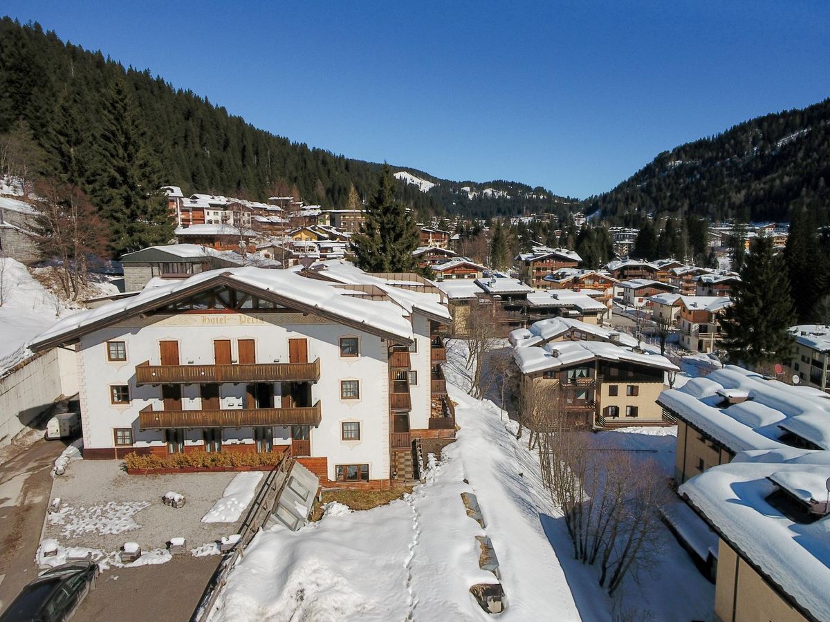 Hotel Perla immerso nella neve a Madonna di Campiglio, con cielo azzurro e le vette delle Dolomiti di Brenta sullo sfondo