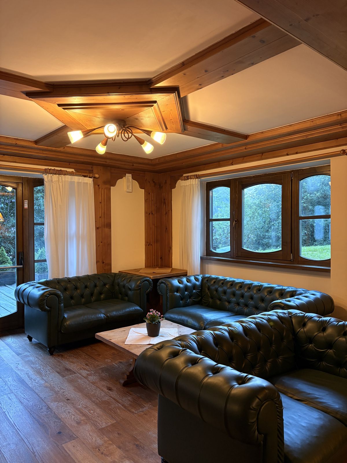 Salotto di Hotel Perla con divani Chesterfield in pelle verde, soffitto in legno a cassettoni e ampie finestre sul verde